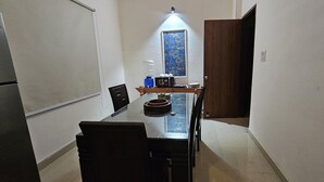A narrow kitchen with a refrigerator, a water dispenser, a microwave, and a window with a floral pattern. - Bunk house villa (Noida)