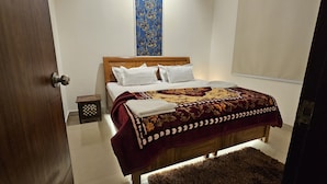 A neatly made bed with a patterned bedspread, a wooden headboard, and white pillows. - Bunk house villa (Noida)