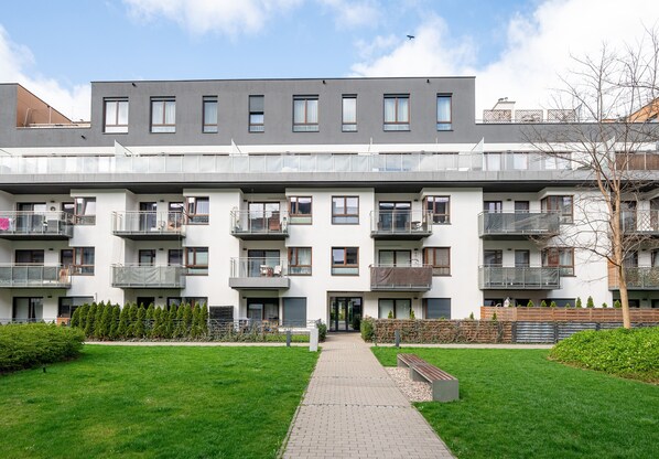 A modern multi-story residential building with balconies, a central entrance, and a well-maintained lawn.
