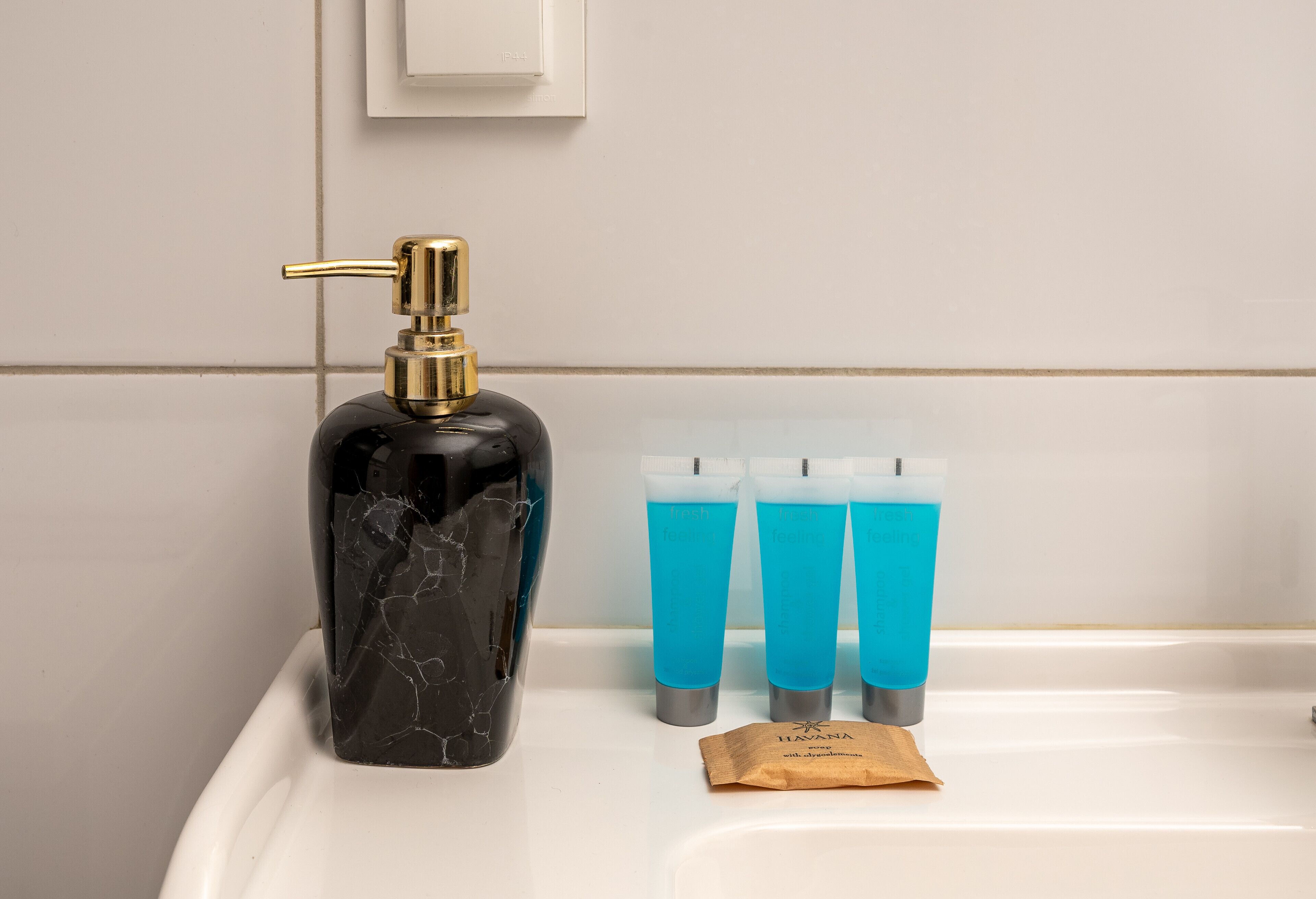 A bathroom with a marble soap dispenser, three blue tubes of liquid soap, and a brown tissue packet.