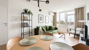 Een moderne woonkamer met een groene bank, een houten eettafel en een boekenkast.