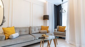 Een moderne woonkamer met een grijze bank, gele kussens, een glazen salontafel en een vloerlamp.