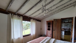 Un dormitorio con cama, ventana con cortinas, armario de madera y una araña.