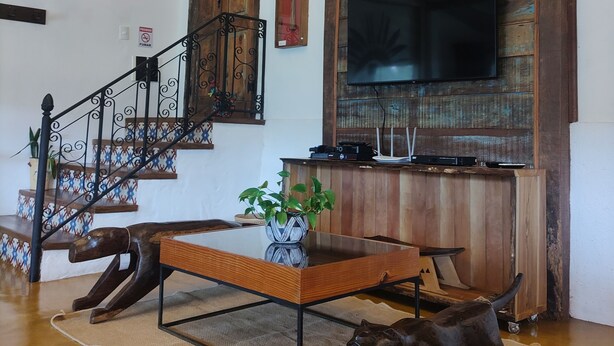 Una sala de estar con una escalera de madera, un televisor de pantalla plana montado en una pared de madera y una escultura decorativa de un oso en el suelo.