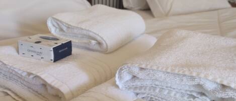 A neatly made bed with folded towels and a box of toiletries.
