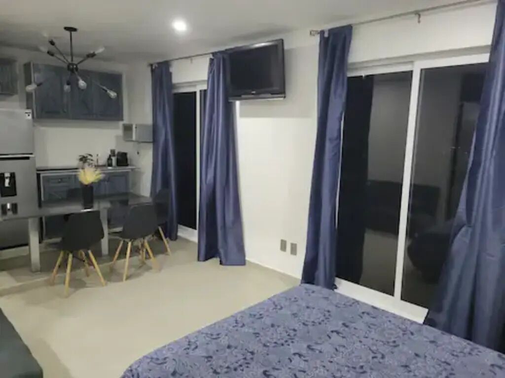 Ein Schlafzimmer mit Bett, Schreibtisch und Stuhl. An der Wand ist ein Fernseher und es gibt eine Schiebetür.