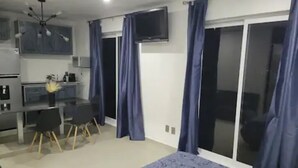 A bedroom with a bed, a desk, and a chair. There is a television on the wall and a sliding door.