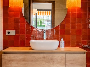 A bathroom with a white sink, a mirror, and red-tiled walls.