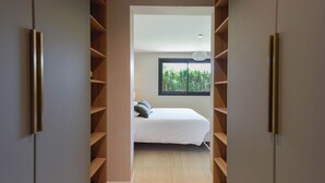 A bedroom with a bed, a window with a view of greenery, and a closet with shelves.