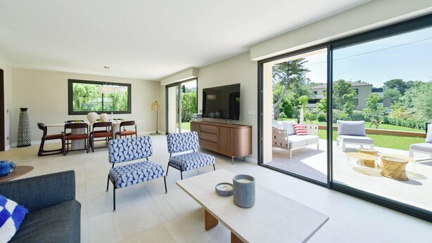 A modern living room with a dining area, large windows, and a view of the outdoors.