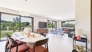 A modern living room with a dining area, large windows, and a flat-screen TV.
