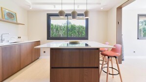 A modern kitchen with a central island, pendant lights, and a large window with a view of greenery.