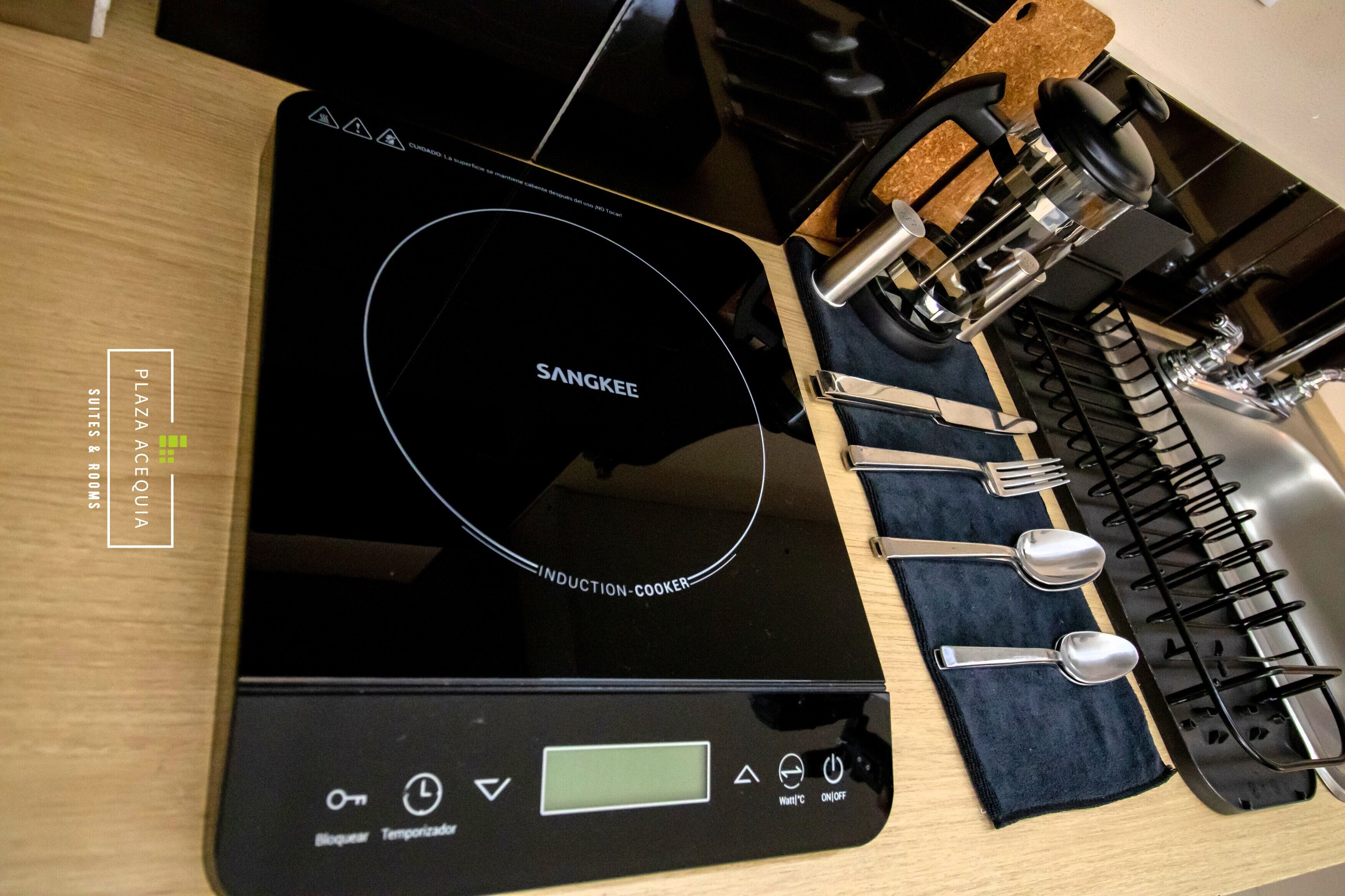 Una placa de inducción negra con pantalla digital y panel de control, una estufa a gas con un tapete de corcho y un bloque para cuchillos con utensilios.