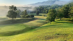 Een golfbaan met glooiende heuvels, bomen en bergen op de achtergrond.