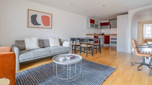 Una sala de estar moderna con un sofá gris, una mesa de centro y un comedor con una mesita y sillas.