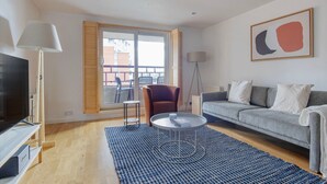 Una sala de estar moderna con un sofá gris, una mesa de centro redonda, un tapete azul estampado, un televisor y una lámpara de pie.