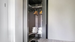 A narrow hallway with a grey wall, a wooden table at the end, and a shelf with folded towels and wooden hangers.