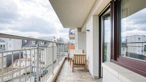 A balcony with a chair and a table, a view of the street, and a building in the background.