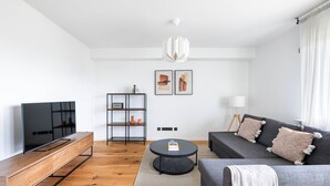 A modern living room with a flat-screen TV, wooden entertainment unit, grey sofa, round coffee table, and a bookshelf with decorative items.