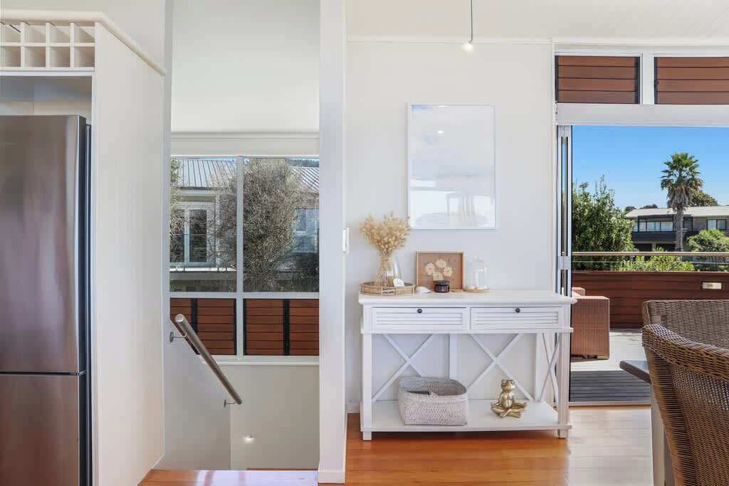 A modern kitchen with a stainless steel refrigerator, a white console table with decorative items, and a wicker chair.
