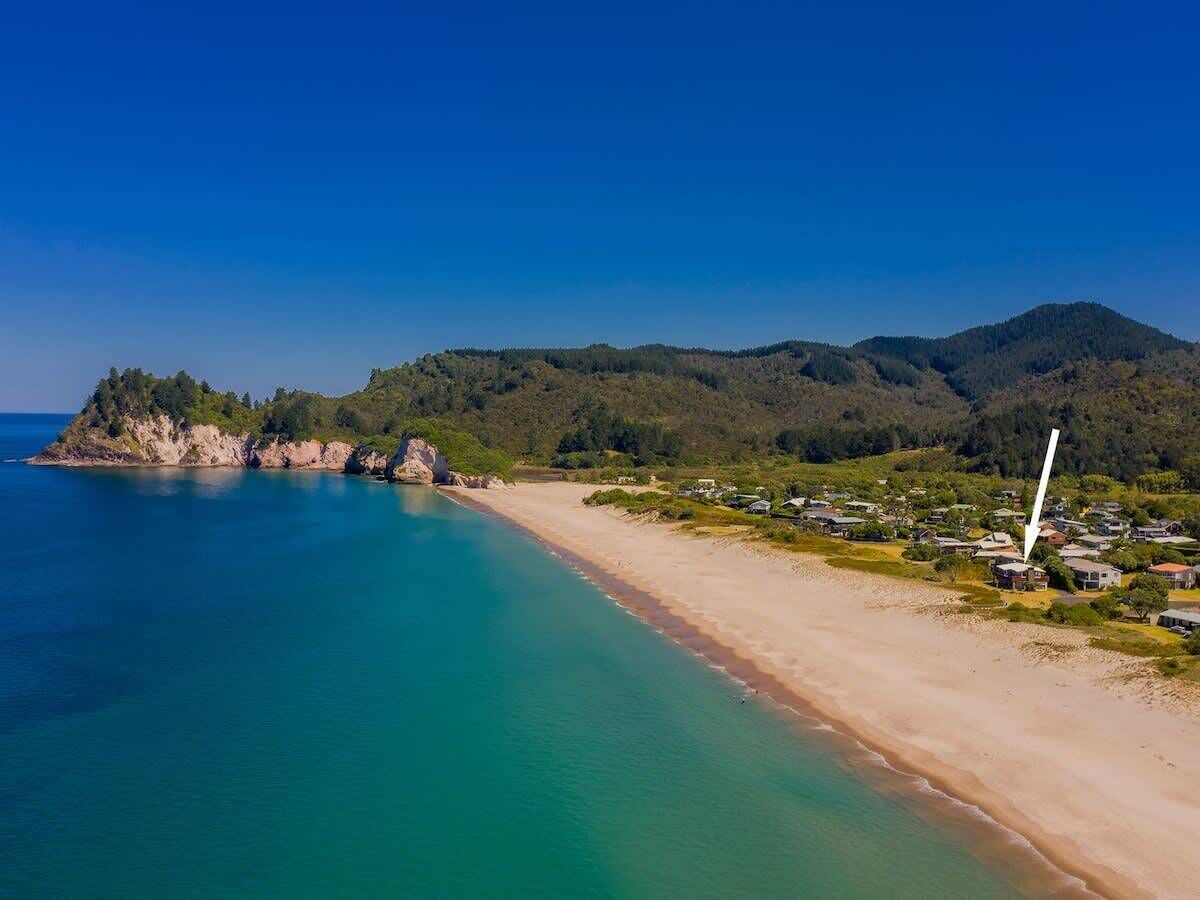 Kystlandskab med strand, klart blåt vand og et boligområde med huse.