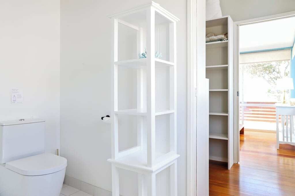 Un bagno con il water, un armadietto bianco e un'apertura che dà su una stanza con pavimento in legno.
