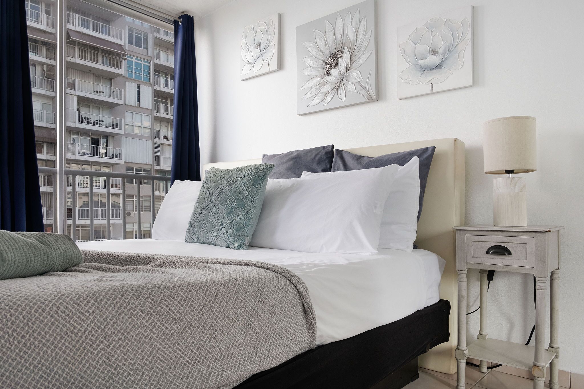 Un dormitorio con una cama, una mesita de noche con una lámpara y una obra de arte en la pared.