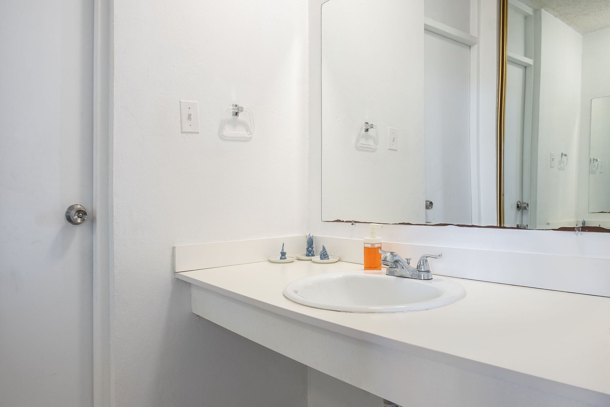 Une salle de bain avec un lavabo blanc, un miroir et une porte.