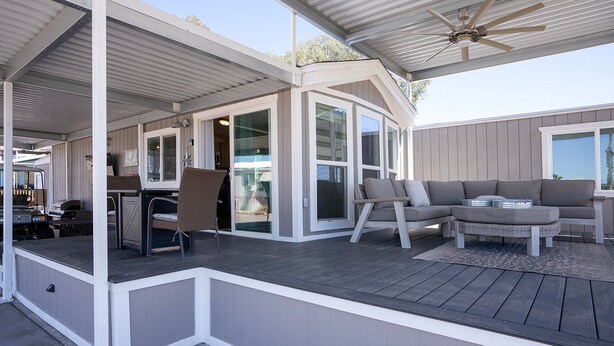 Un espacio al aire libre cubierto con una terraza de madera, una zona de estar con sofá y sillones, y un ventilador de techo.