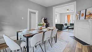 A spacious dining area with a wooden table set for four, surrounded by chairs. There is a sofa and a fireplace in the background. - Modern Luxury Retreat |Pet-Friendly |Hot Tub |BBQ (St. Louis)