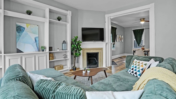 A living room with a fireplace, green upholstered sofas, a flat-screen TV, and white shelving units. - Modern Luxury Retreat |Pet-Friendly |Hot Tub |BBQ (St. Louis)
