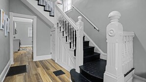 A staircase with white balusters and black steps, leading to a landing with a door and a vent. - Modern Luxury Retreat |Pet-Friendly |Hot Tub |BBQ (St. Louis)