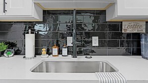 A modern kitchen with a stainless steel sink, a black tiled backsplash, and a sign that reads "HELP YOURSELF coffee BAR". - Modern Luxury Retreat |Pet-Friendly |Hot Tub |BBQ (St. Louis)