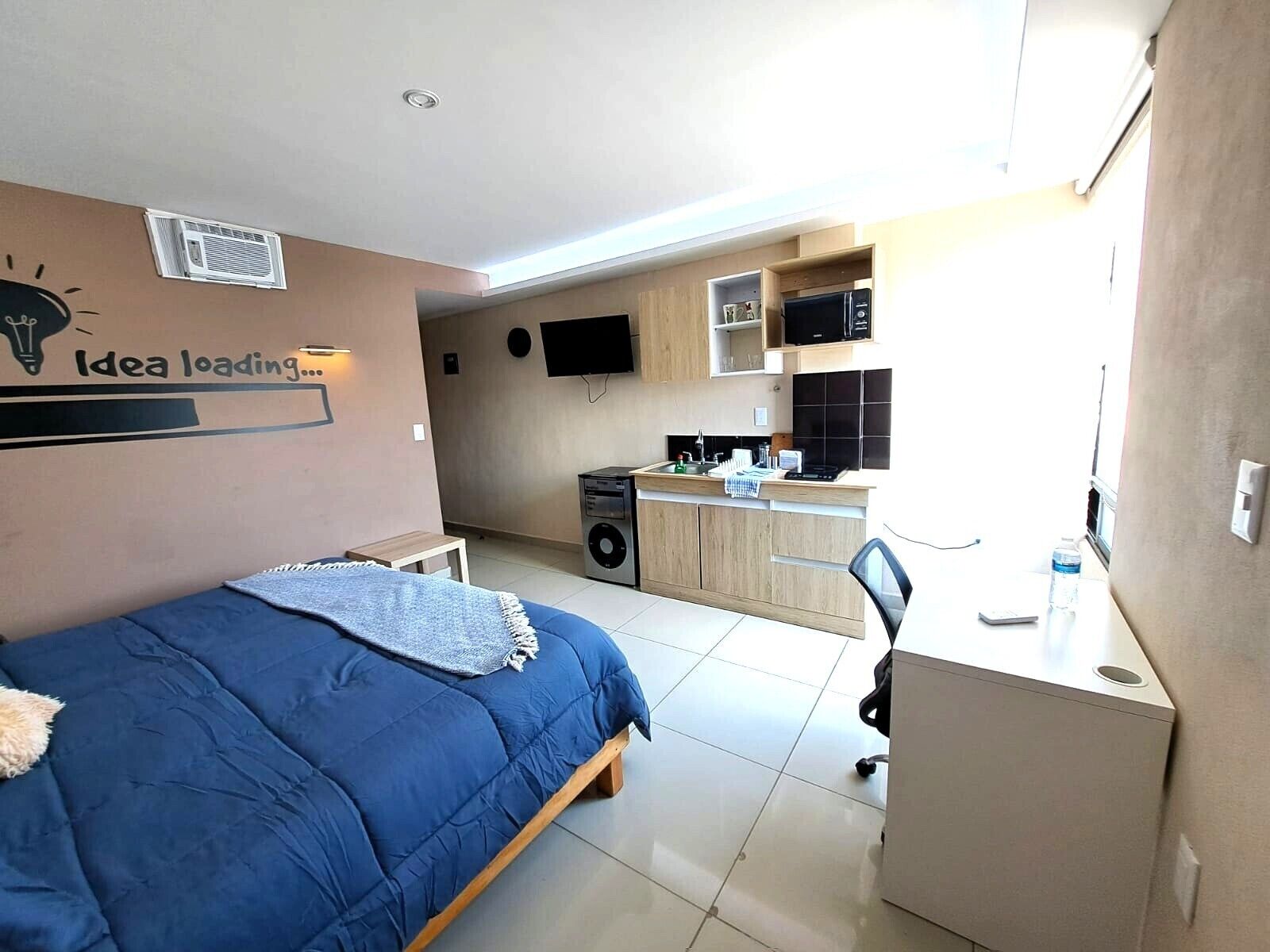 A compact room with a bed, a desk, a kitchenette, and a TV.