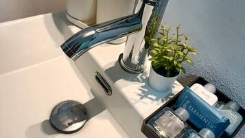 A bathroom sink with a chrome faucet, a small potted plant, and a tray with toiletries.