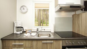 A modern kitchen with a built-in stove, a coffee maker, a sink, and a window with a view of trees. - Kleines Aber Feines Ferienhäuschen in Strandnähe - Tiny Chalet Nr. 816 - Tiny Chalets (Binz)