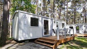 A white mobile home with a deck, a window, and a door. - Kleines Aber Feines Ferienhäuschen in Strandnähe - Tiny Chalet Nr. 819 - Tiny Chalets (Binz)