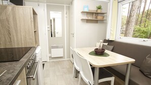 A compact kitchen with a dining area, a built-in stove, and a window with a view of trees. - Kleines Aber Feines Ferienhäuschen in Strandnähe - Tiny Chalet Nr. 819 - Tiny Chalets (Binz)