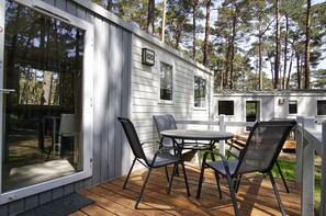 Une maison mobile dotée d’une terrasse, d’un espace salon extérieur et d’une grande fenêtre.