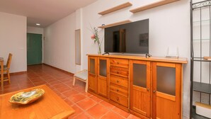 A room with a wooden cabinet, a television, and a dining table with a vase of flowers. - OASIS PLAYERO - Nice flat with shared pool and Free Wifi (Chiclana de la Frontera)
