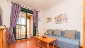 A small, cozy room with a sofa, a wooden table, and purple curtains. - OASIS PLAYERO - Nice flat with shared pool and Free Wifi (Chiclana de la Frontera)