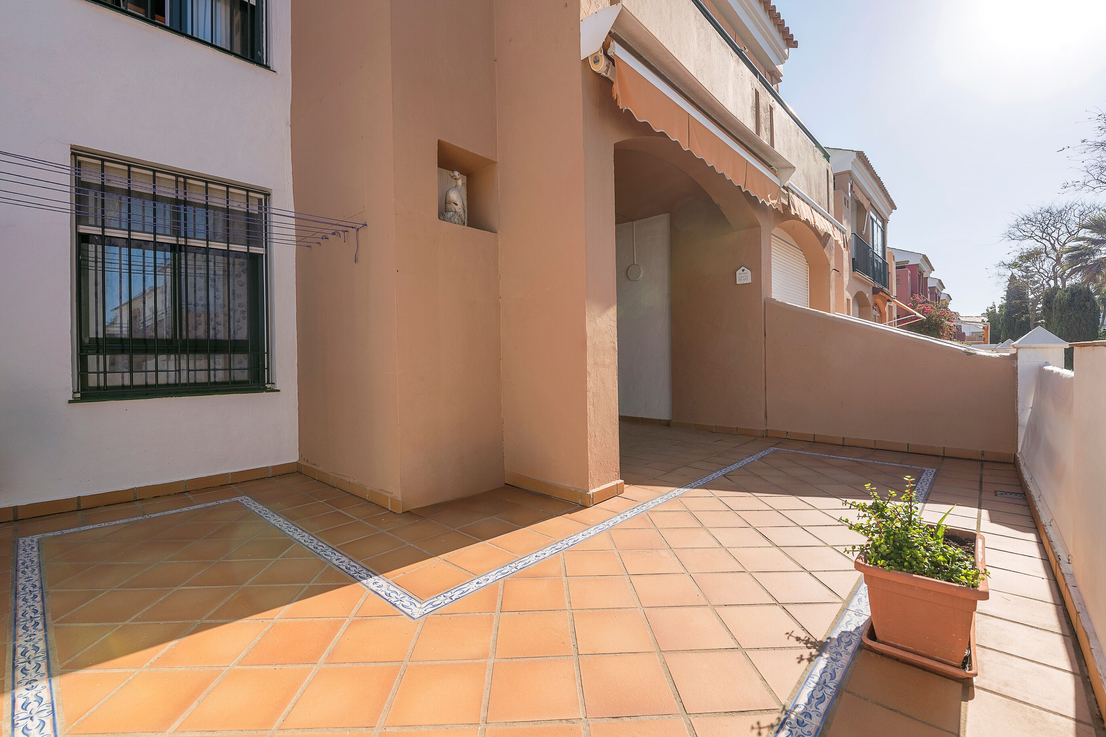 Un edificio residencial con un patio empedrado, una planta en maceta y una ventana con reja de metal.
