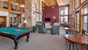 Un espace intérieur spacieux comprenant une table de billard, des sièges confortables et de grandes fenêtres.