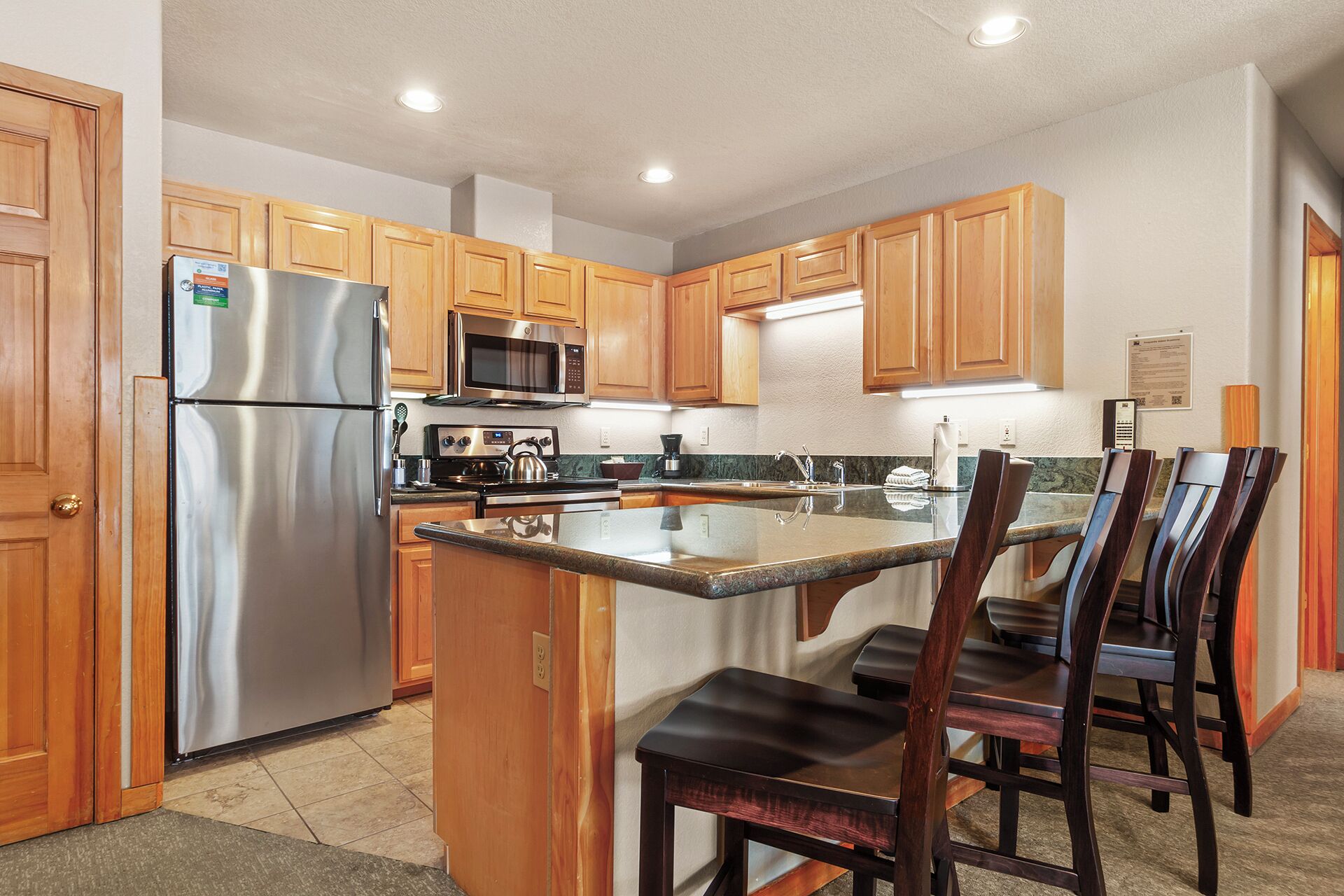A kitchen with wooden cabinets, stainless steel appliances, a granite countertop, and a dining area with wooden chairs.