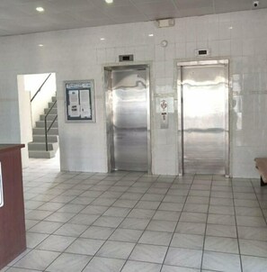 Egy előtér, amelyben két lift, egy lépcsőház és egy hirdetőtábla található.