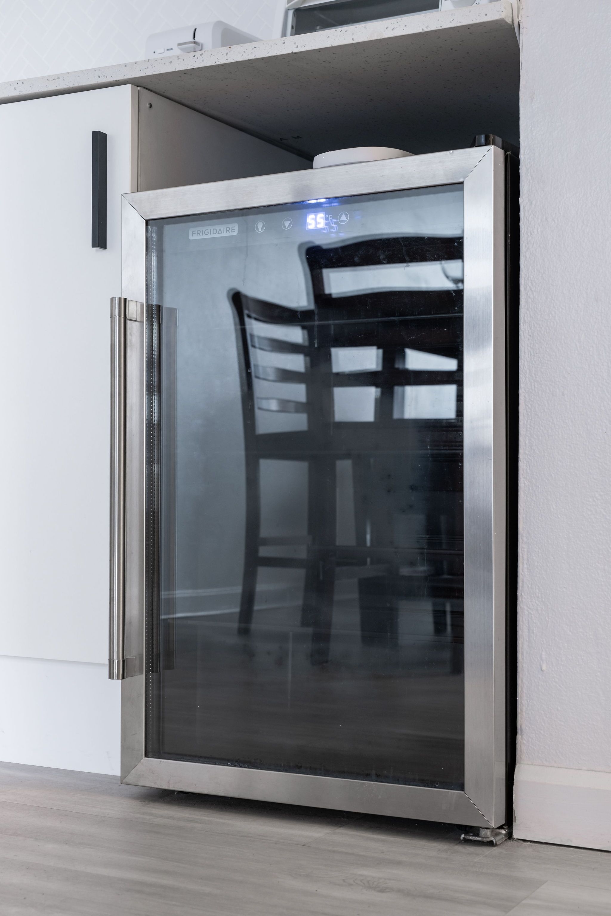 Una cocina moderna con un refrigerador de acero inoxidable, una silla de madera y una pared blanca.