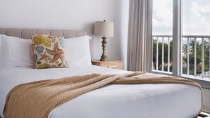 A hotel room with a bed, a ceiling fan, a nightstand with a lamp, and a view of the outdoors through a large window. - MEDIA LUNA STUDIO OCEANVIEW (Carolina)