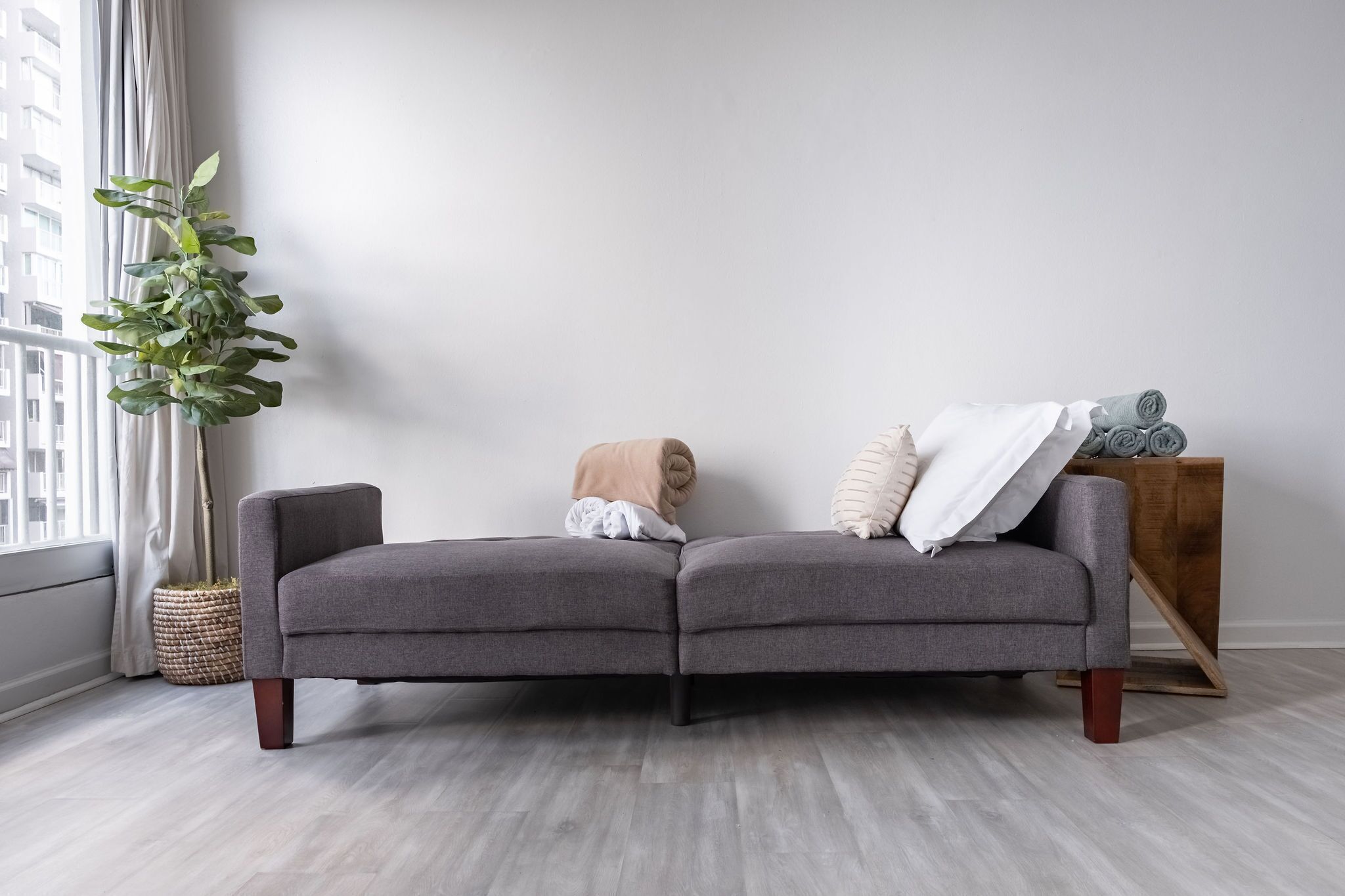Una sala de estar moderna con un sofá seccional gris, una mesita auxiliar, una planta en maceta y un ventanal con cortinas.