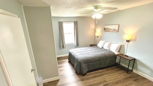 A bedroom with a bed, a nightstand, a ceiling fan, and a window with curtains. - Cozy Sleeping Bear Dunes Cabin 1 (Honor)