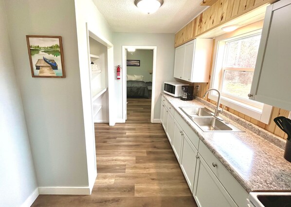 Una cocina con armarios blancos, encimera de granito, microondas y fregadero.
